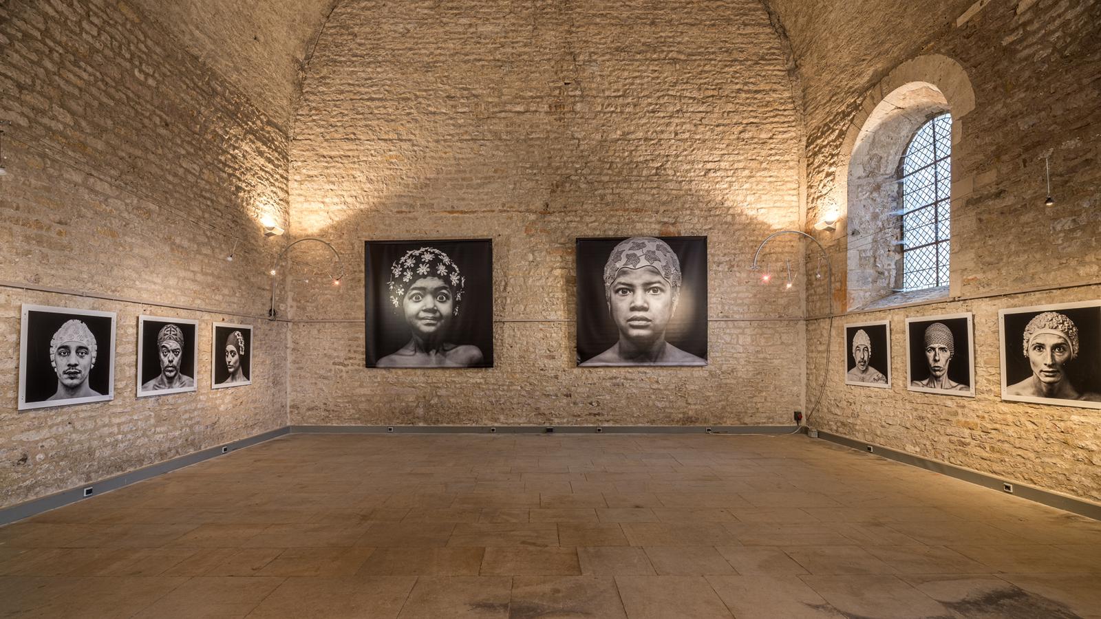 Exposition de portraits accroch&eacute;s dans un espace en pierre.